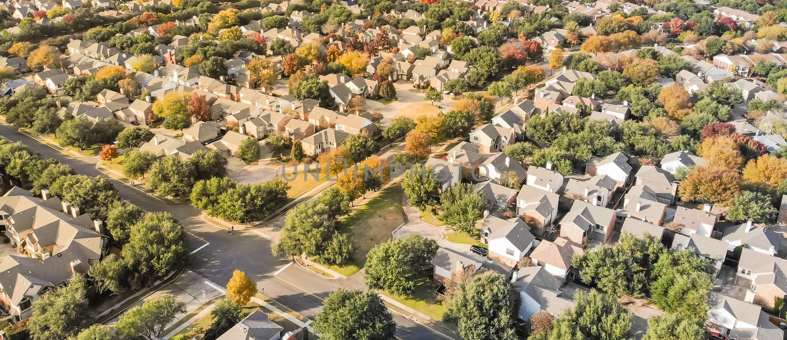 Panorama aerial drone view urban sprawl in suburban Dallas, Texas during fall season with colorful leaves. Flyover subdivision with row of single-family detached houses and apartment complex