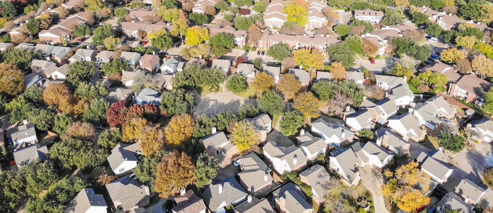 Panorama aerial drone view urban sprawl in suburban Dallas, Texas during fall season with colorful leaves. Flyover subdivision with row of single-family detached houses and apartment complex