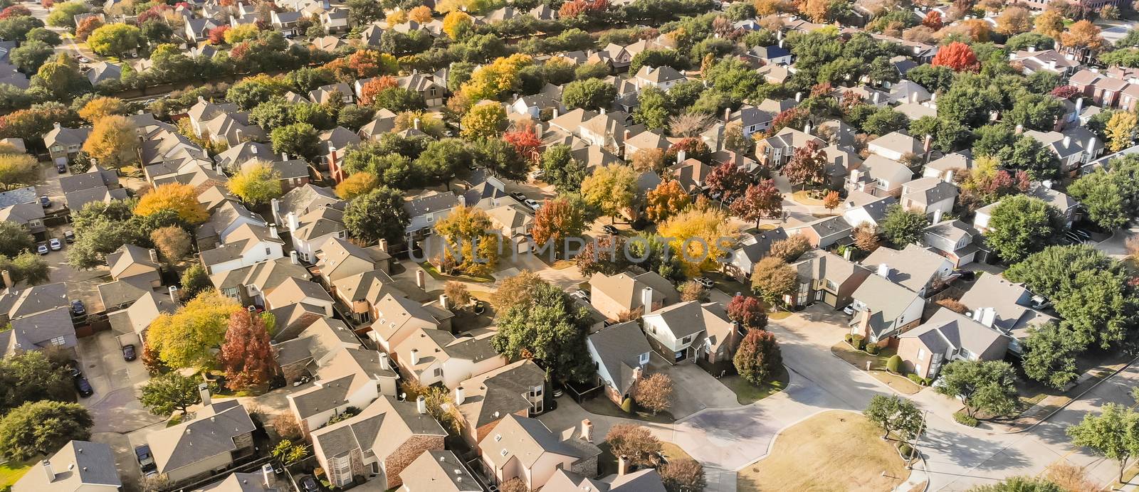 Panorama aerial drone view urban sprawl in suburban Dallas, Texas during fall season with colorful leaves. Flyover subdivision with row of single-family detached houses and apartment complex