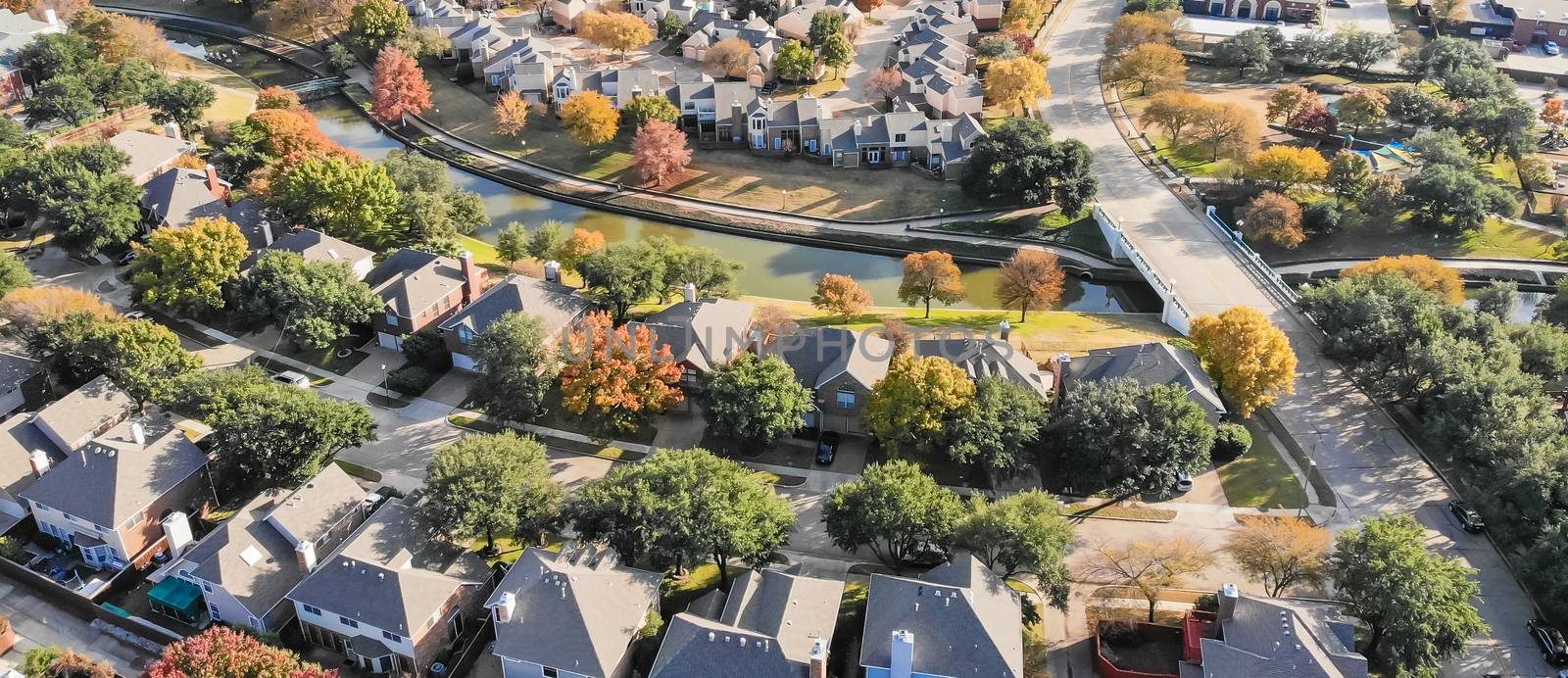 Panorama aerial drone view urban sprawl in suburban Dallas, Texas during fall season with colorful leaves. Flyover subdivision with row of single-family detached houses and apartment complex