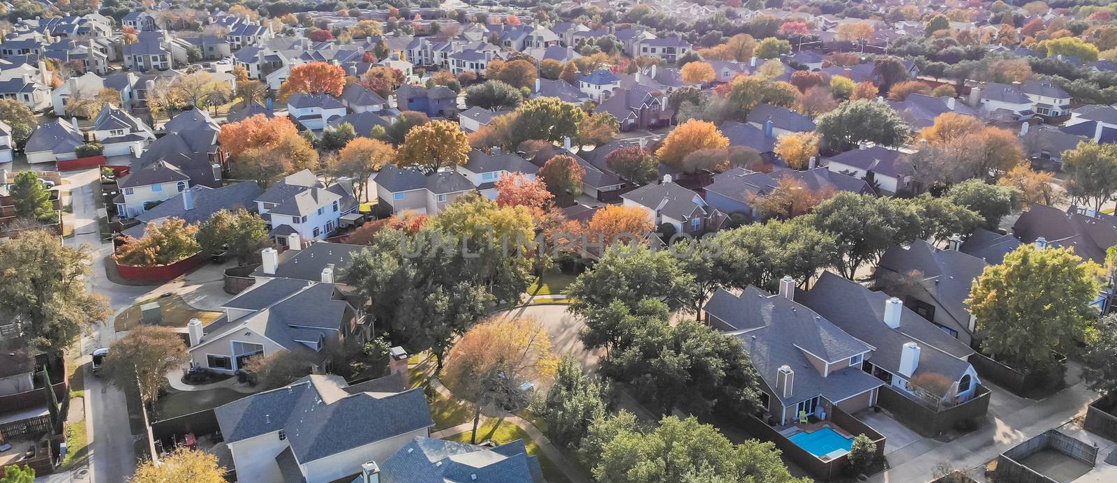 Panorama aerial drone view urban sprawl in suburban Dallas, Texas during fall season with colorful leaves. Flyover subdivision with row of single-family detached houses and apartment complex