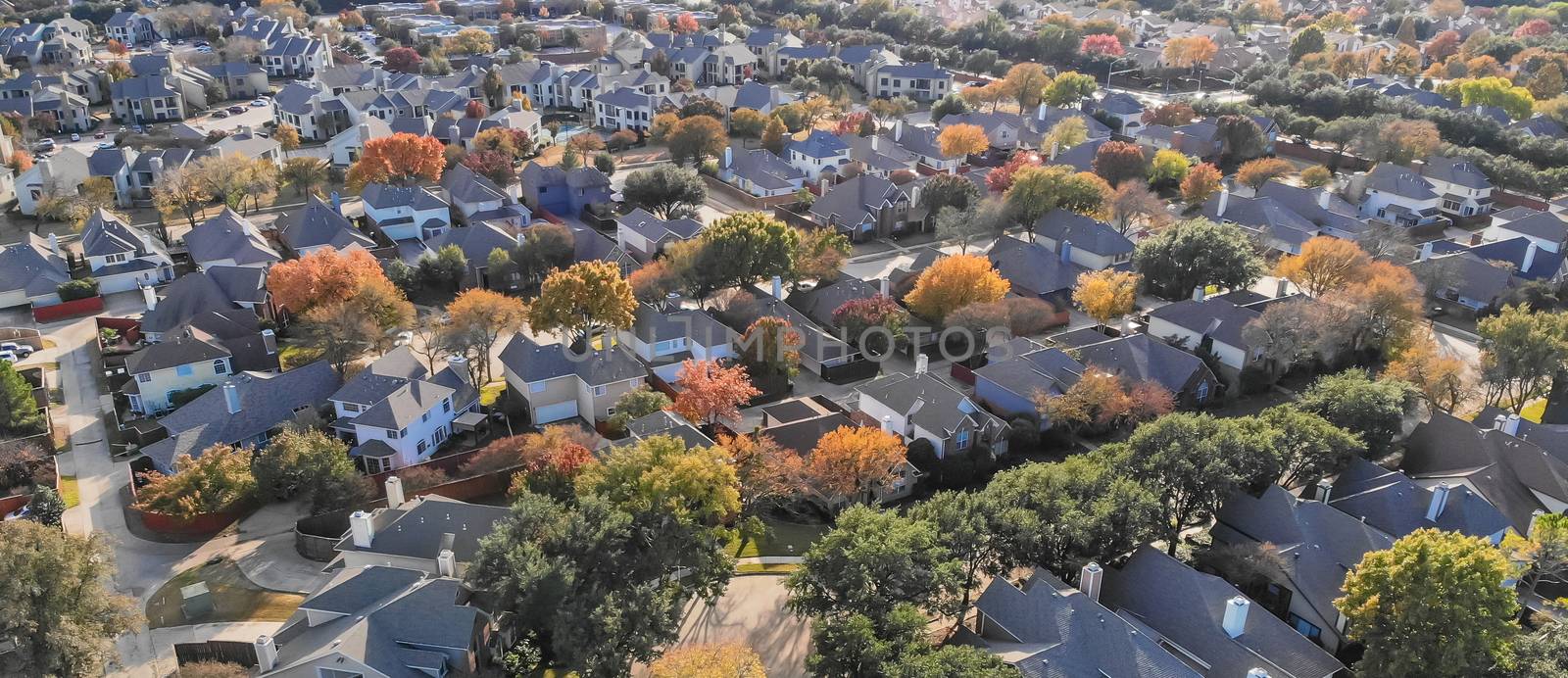 Panorama aerial drone view urban sprawl in suburban Dallas, Texas during fall season with colorful leaves. Flyover subdivision with row of single-family detached houses and apartment complex