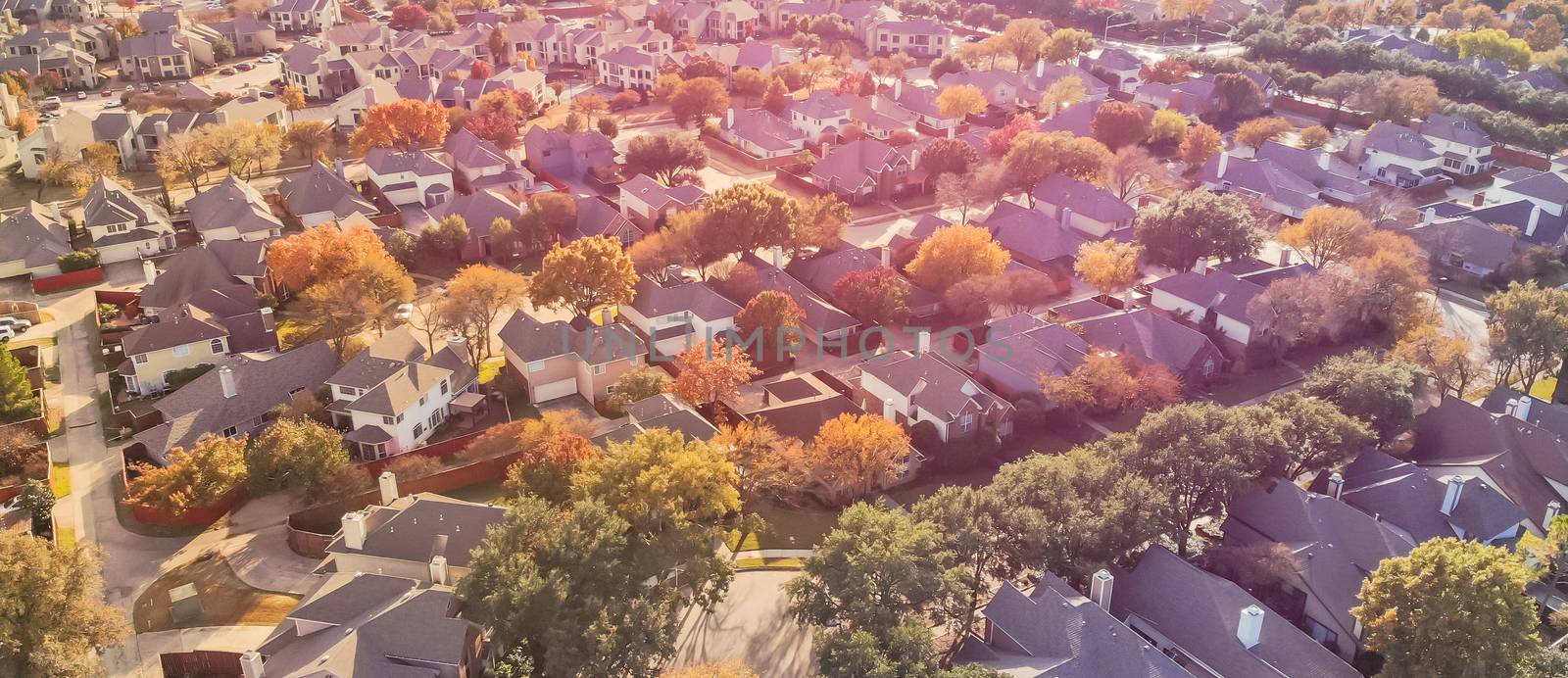 Panorama aerial drone view urban sprawl in suburban Dallas, Texas during fall season with colorful leaves. Flyover subdivision with row of single-family detached houses and apartment complex