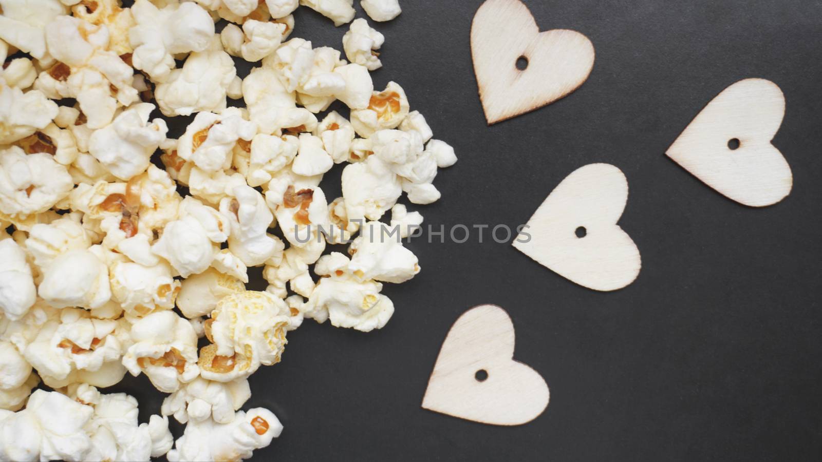 Love popcorn concept. Horizontal photo. Sweet food. Classic salted popcorn with wooden hearts on a black background