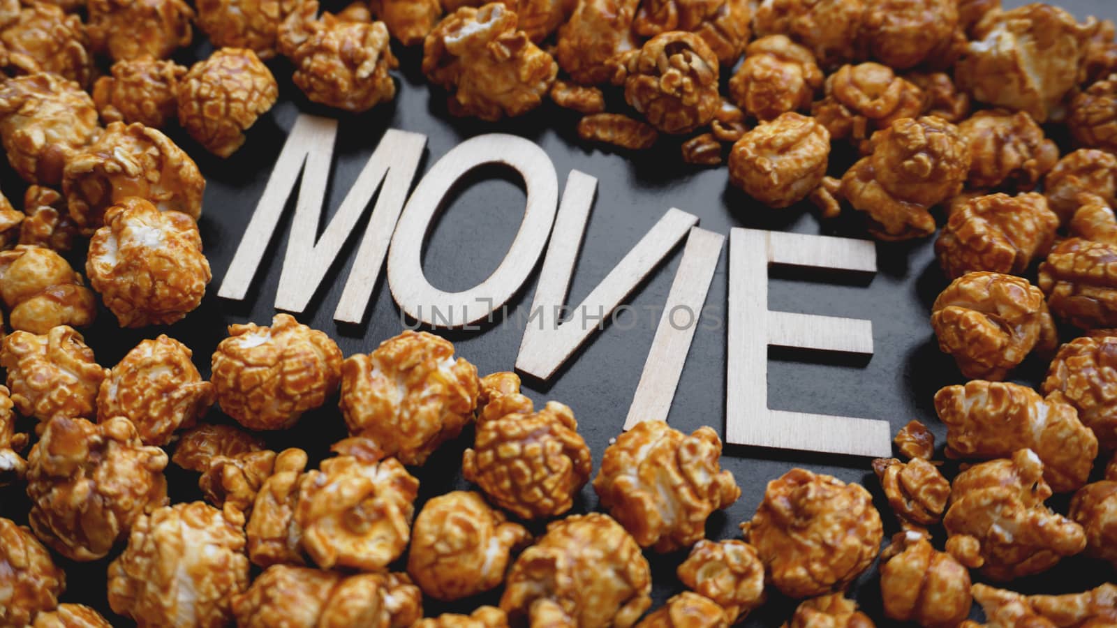 Golden caramel popcorn closeup. Background of popcorn. Snacks and food for a movie. Wooden letters Movie on a black background