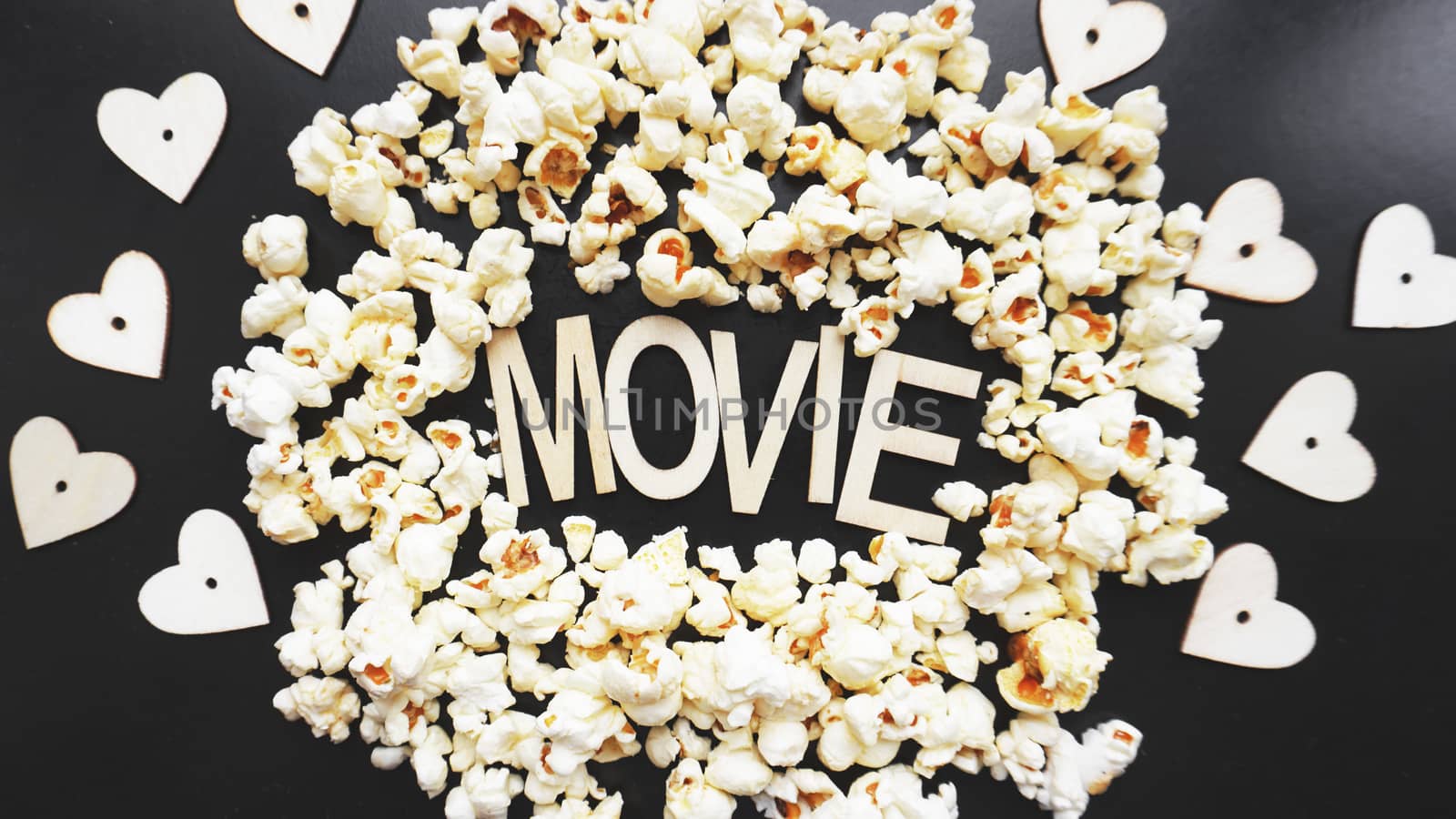 Popcorn on black background. Watching a movie with popcorn. Copy space. Pop corn. Top view. Flat lay. Wooden letters movie with hearts