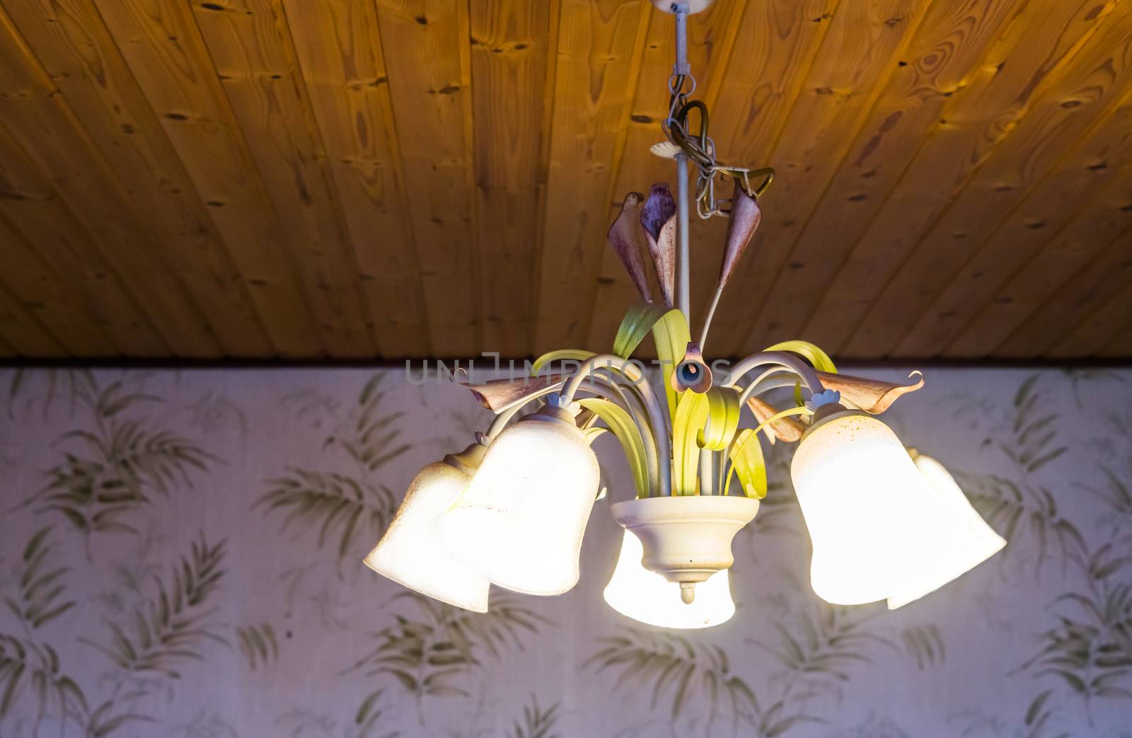 beautiful vintage interior background of a lighted retro chandelier hanging on a wooden ceiling, decorated lamp with flowers, home interior