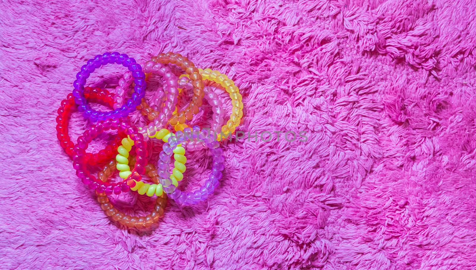 many plastic hair cable elastics in diverse colors isolated on a soft pink background