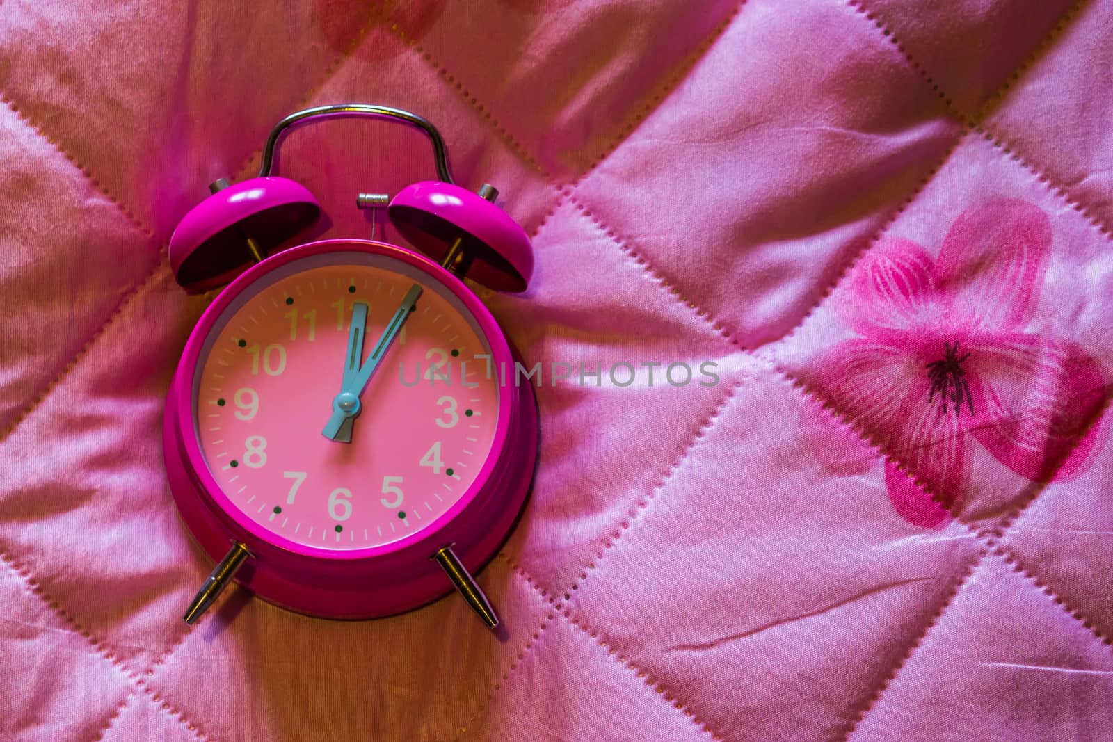 pink girly vintage alarm clock isolated on a pink blanket background