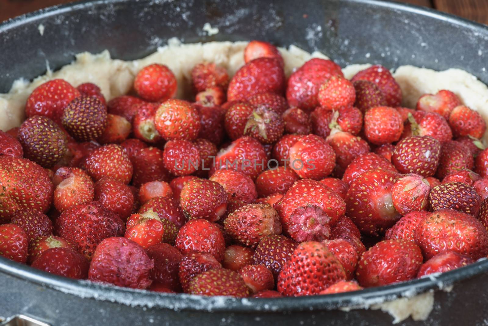 Cooking strawberry cake in metal baking dish on wooden table
