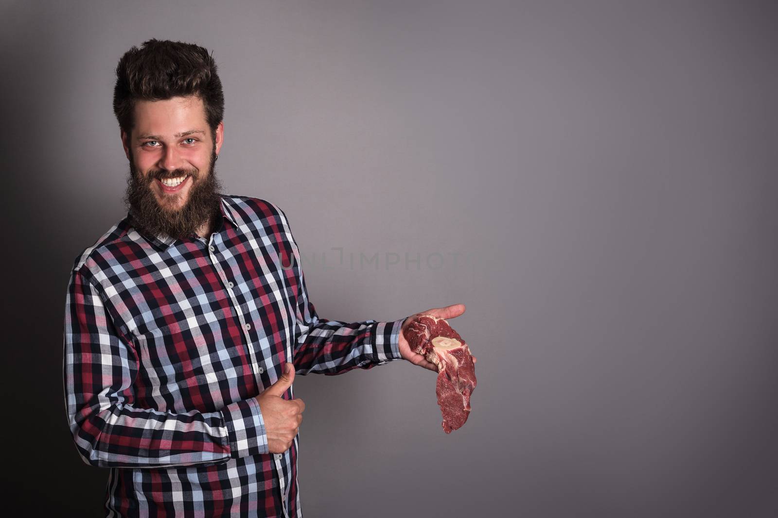 Smiling man holding raw fresh meat and showing thumb up quality concept copy space for text