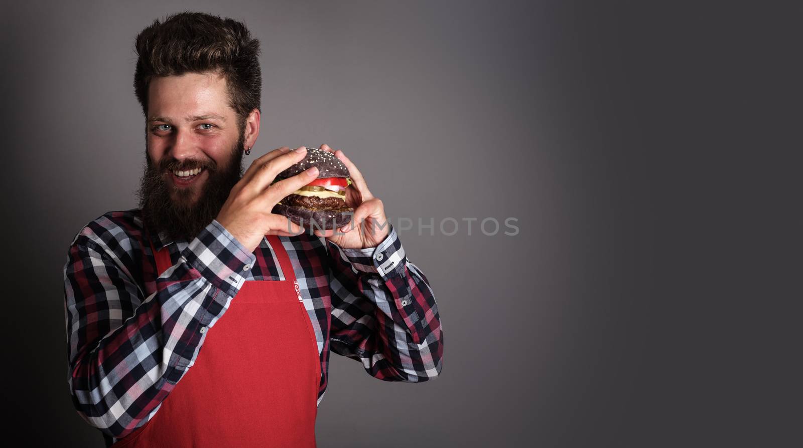 Male cook in red apron giving you fresh self made black burger and smiling