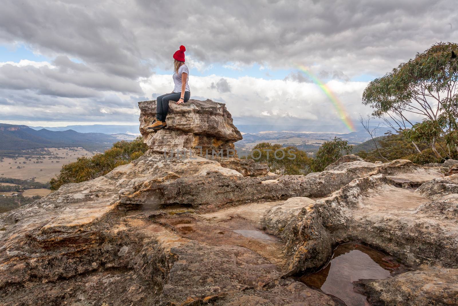 Woman perched on rock pillar peak with the best views below braving the mountain chill by lovleah