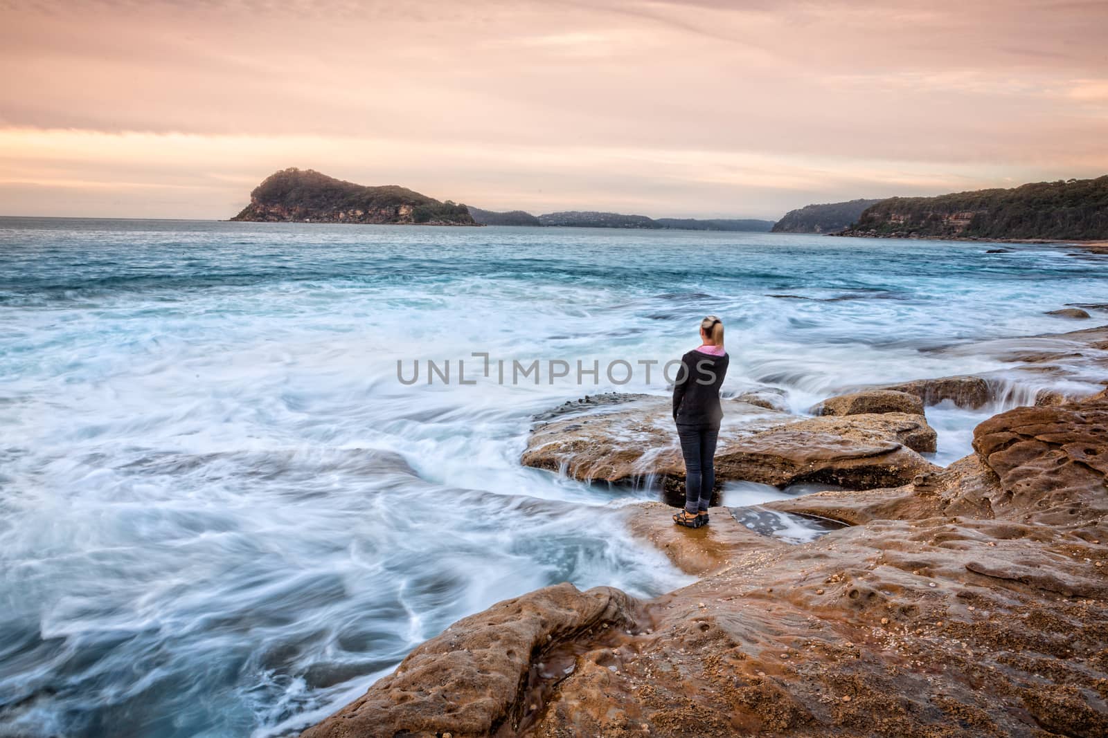 Female standing on rocks letting coastal waves wash up to her feet by lovleah