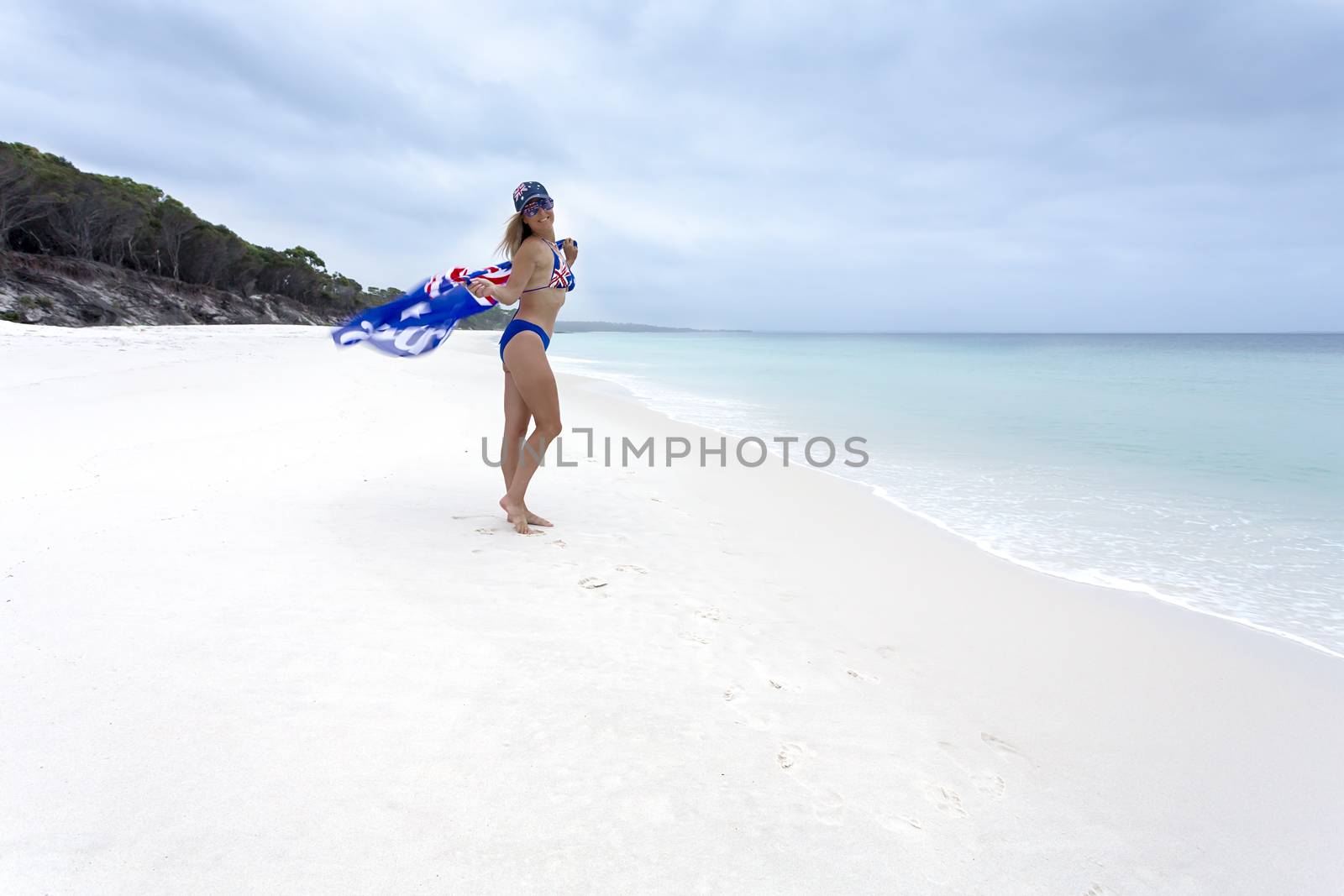 Australian girl holding an Australian flag flapping in the wind. She also wears bikini with Australian flag print and a hat and sunglasses as well. Patriot, Australia Day, Australian travel tourism