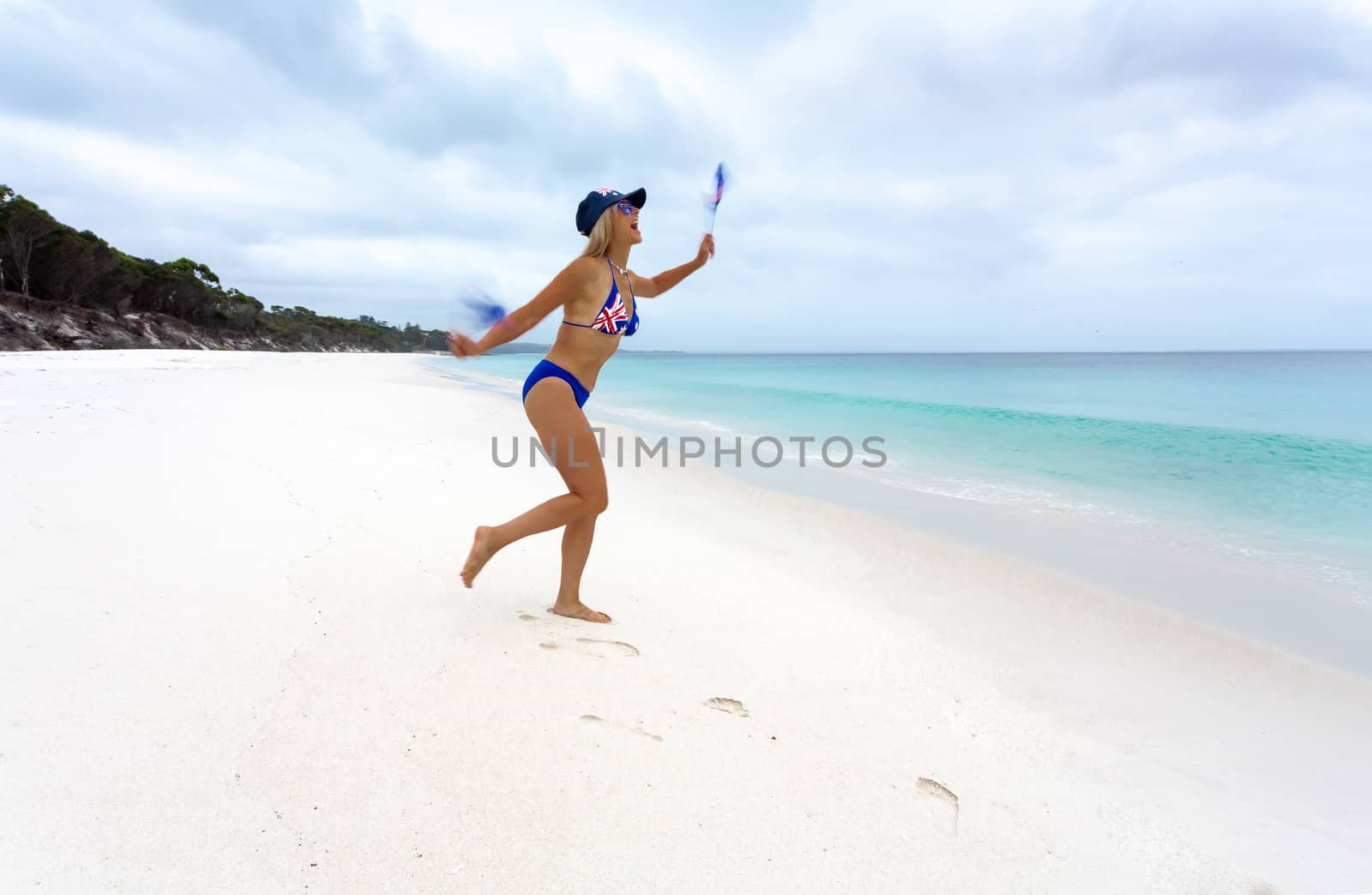 Australian bikini clad woman waving flags with joy on an idyllic pristine beach in Australia. Australia Day celebrations or travel and tourism, space for copy