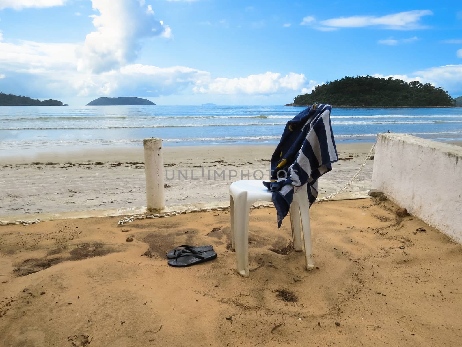 View of the quiet and deserted beach in sunny day, with a chair and a towel.