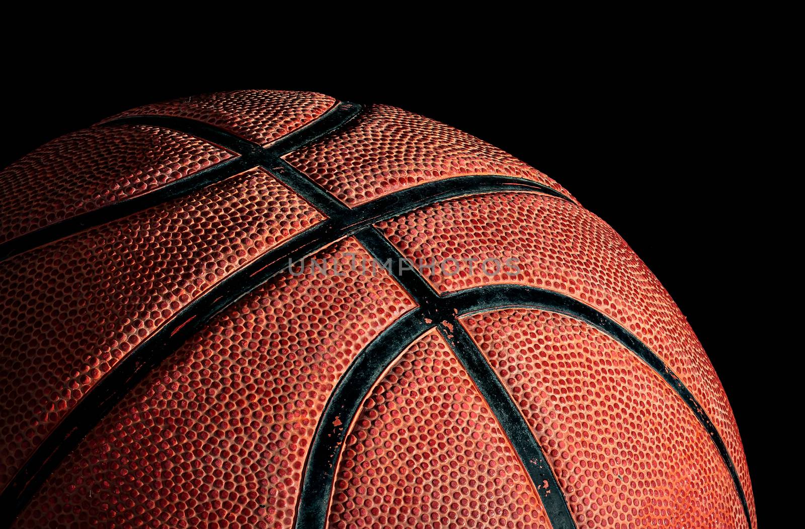 Part of basketball ball illuminated from above. On a black background. Side view.