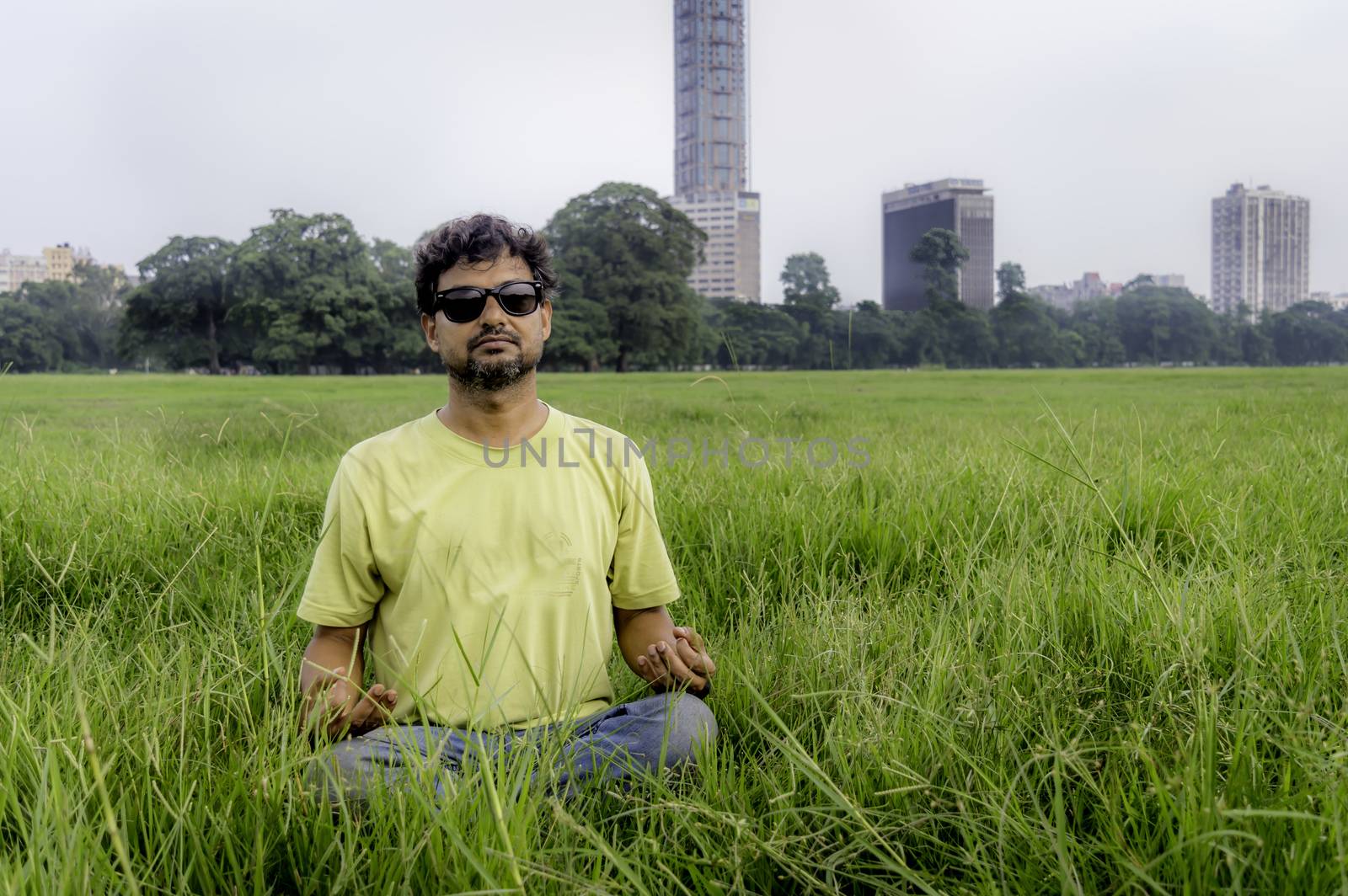 Yoga at park. Senior bearded man in lotus pose sitting on green grass. Concept of calm and meditation.Young man in sunglasses meditating outdoors in the park. ( Moidan, Kolkata, India)