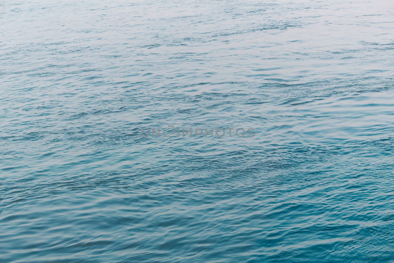 View of Clean flowing blue water surface with ripples and sunrays or sunlight reflections. Beautiful Adriatic Sea water shines at dusk light.Natural beauty Wave water texture design for background.