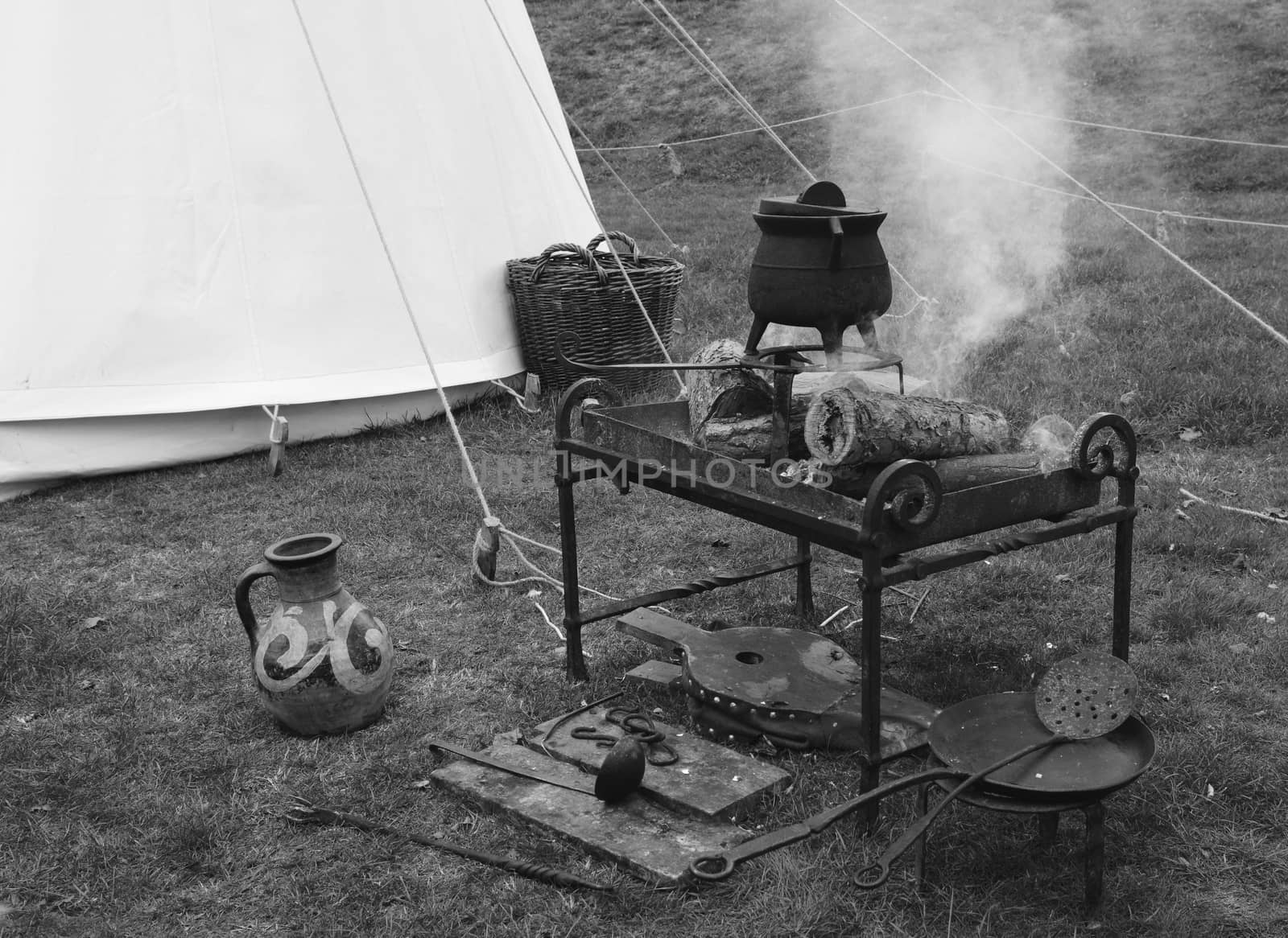 Campfire stove at a Medieval fair with a cast iron pot, bellows and utensils - monochrome processing