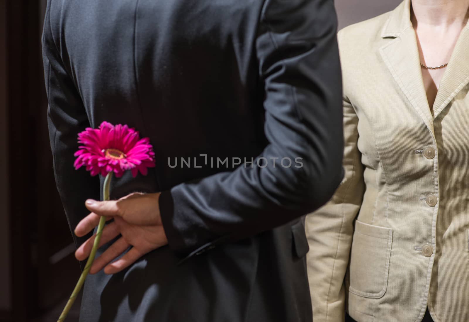 A young man in a suit holds a gerbera flower behind his back, a surprise for a woman, March 8.