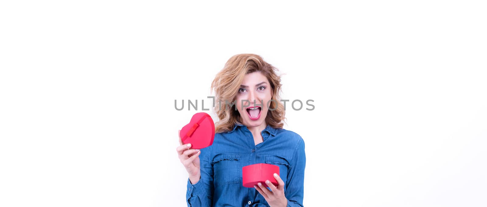 Attractive beautiful model woman gets surprised after opens heart shaped gift box.Valentine's Day concept in studio on a white background.
