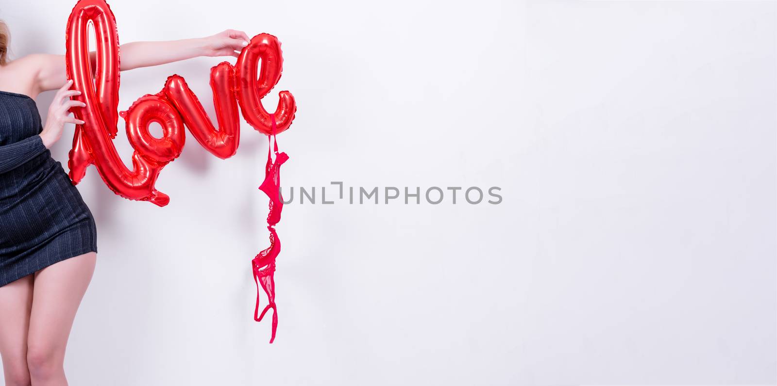 Attractive beautiful model woman holds love word letter shaped red balloon and red lingerie.Valentine's Day concept in studio on a white background.