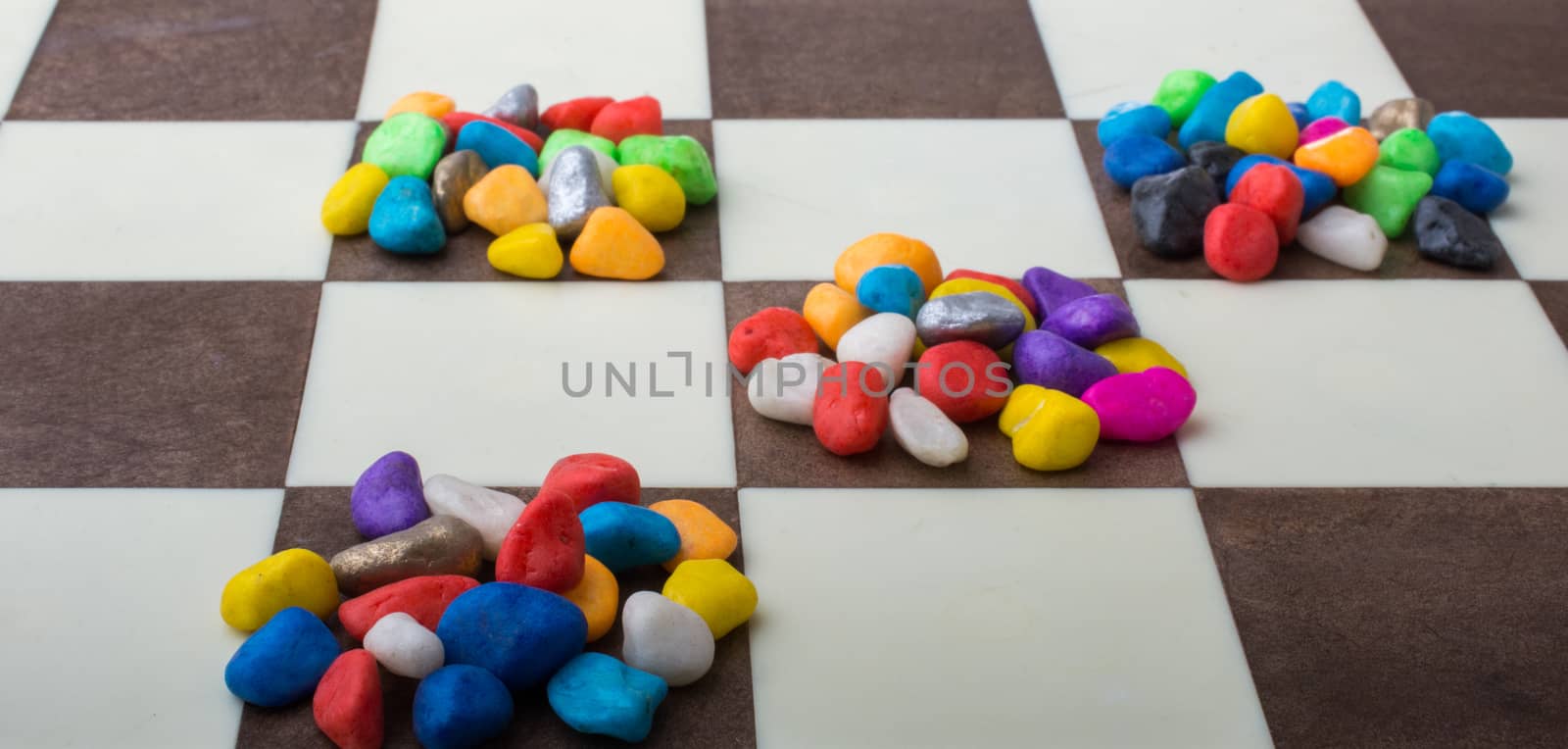 Colorful pebbles spread on checked board  by berkay