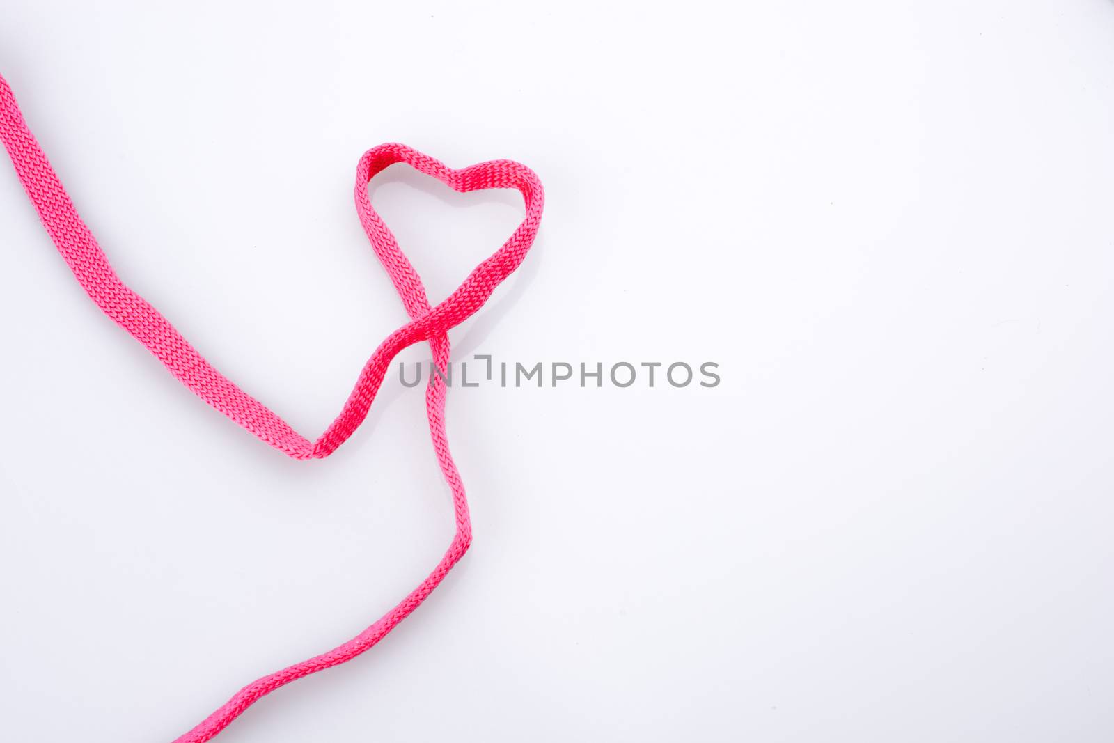 Heart shaped made by the help of a pink sholace on white background