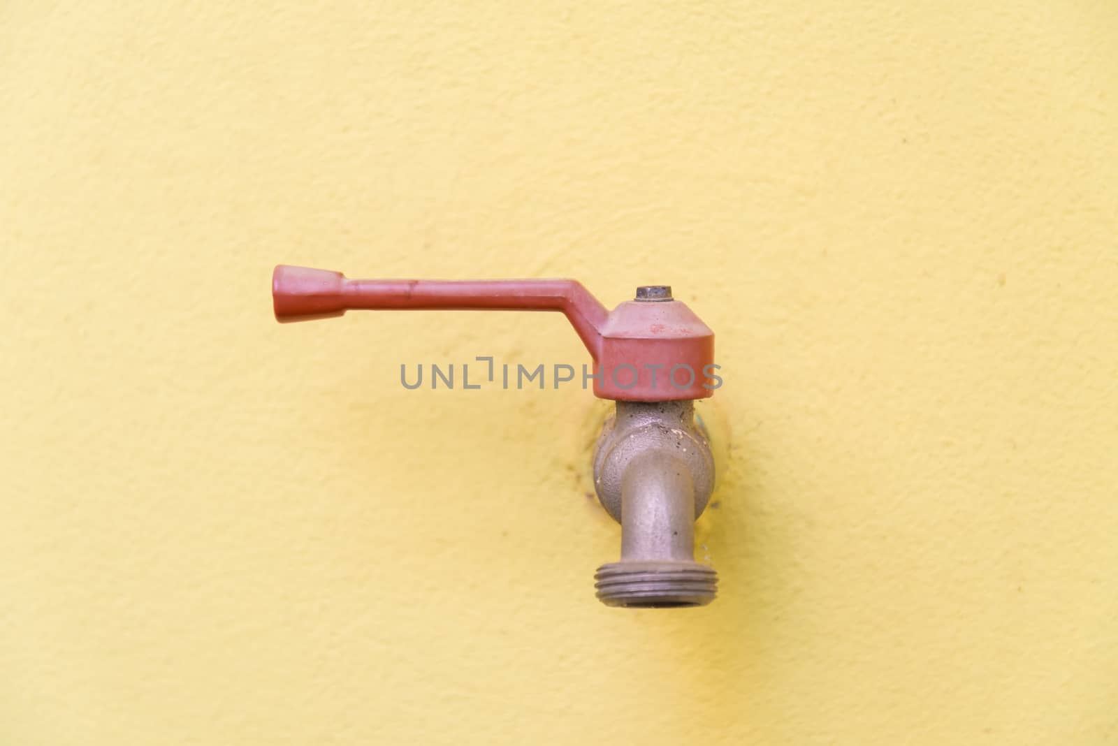 Red faucet on a yellow wall background.