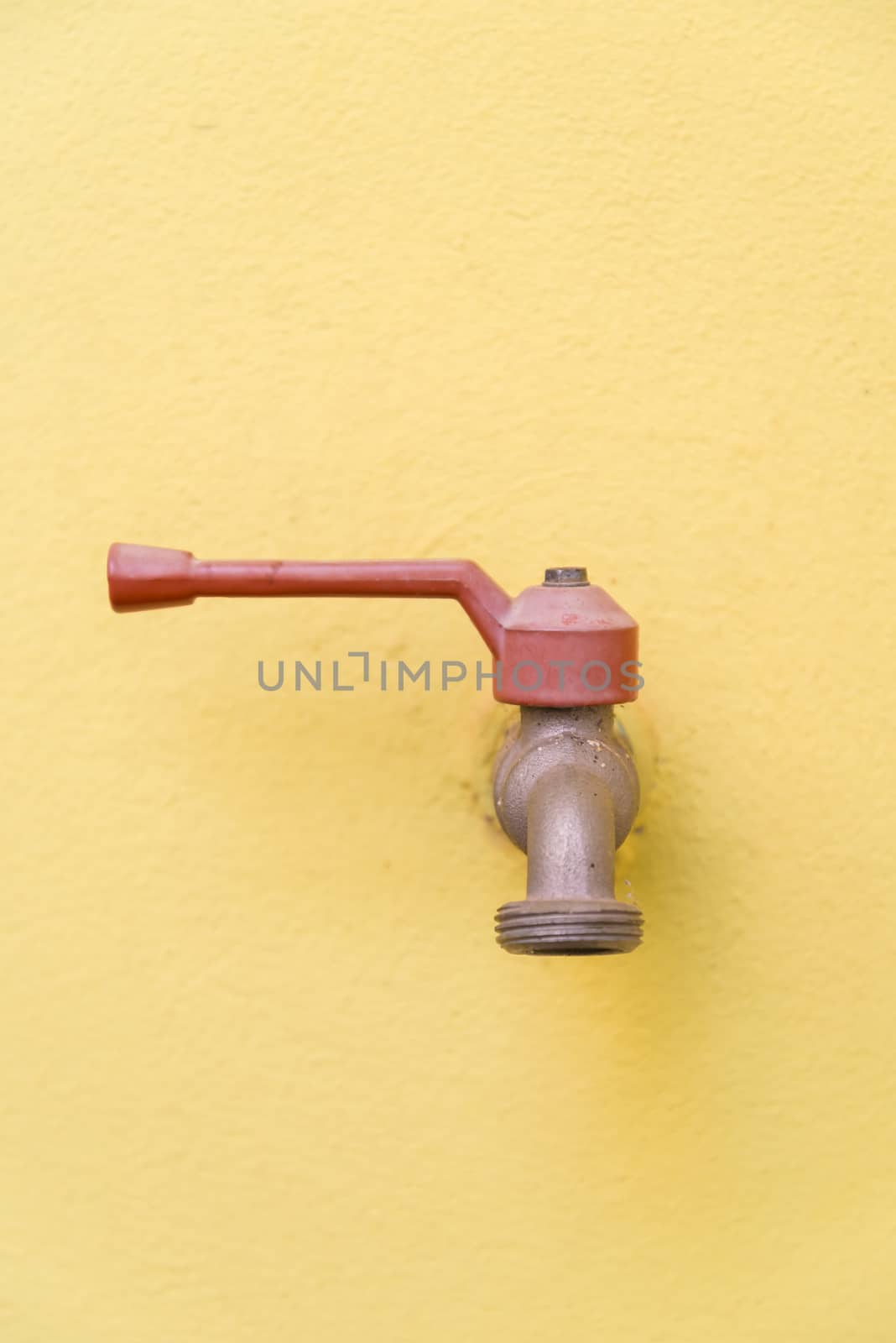 Red faucet on a yellow wall background.