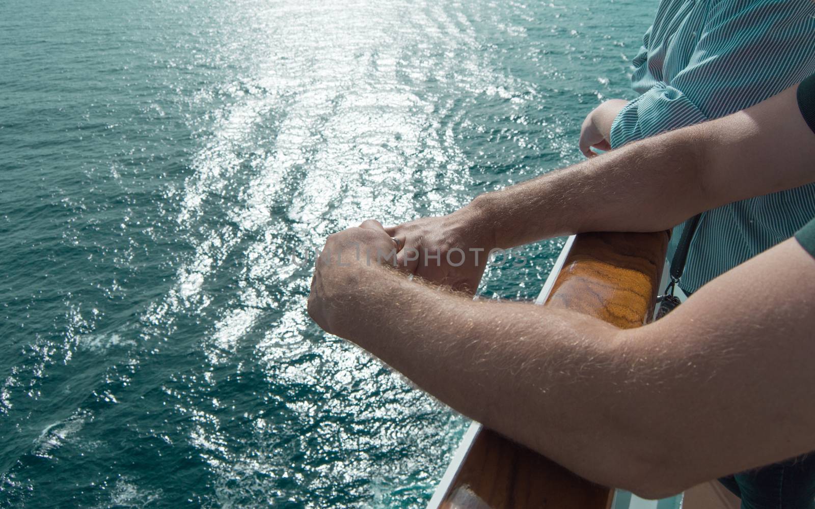 The concept of sea cruises. Men's hands on the railing of the cruise ship on the background of the sea waves and sunset by claire_lucia