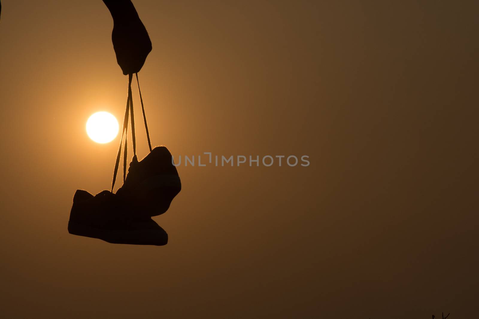 The Boy standing at sunset and holding shoes in his hand. Close-up