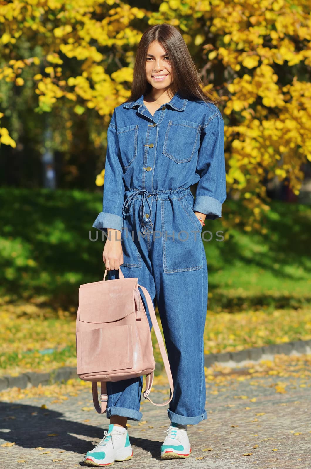 Girl denim clothes holding a pink backpack on a background of yellow autumn in the campus