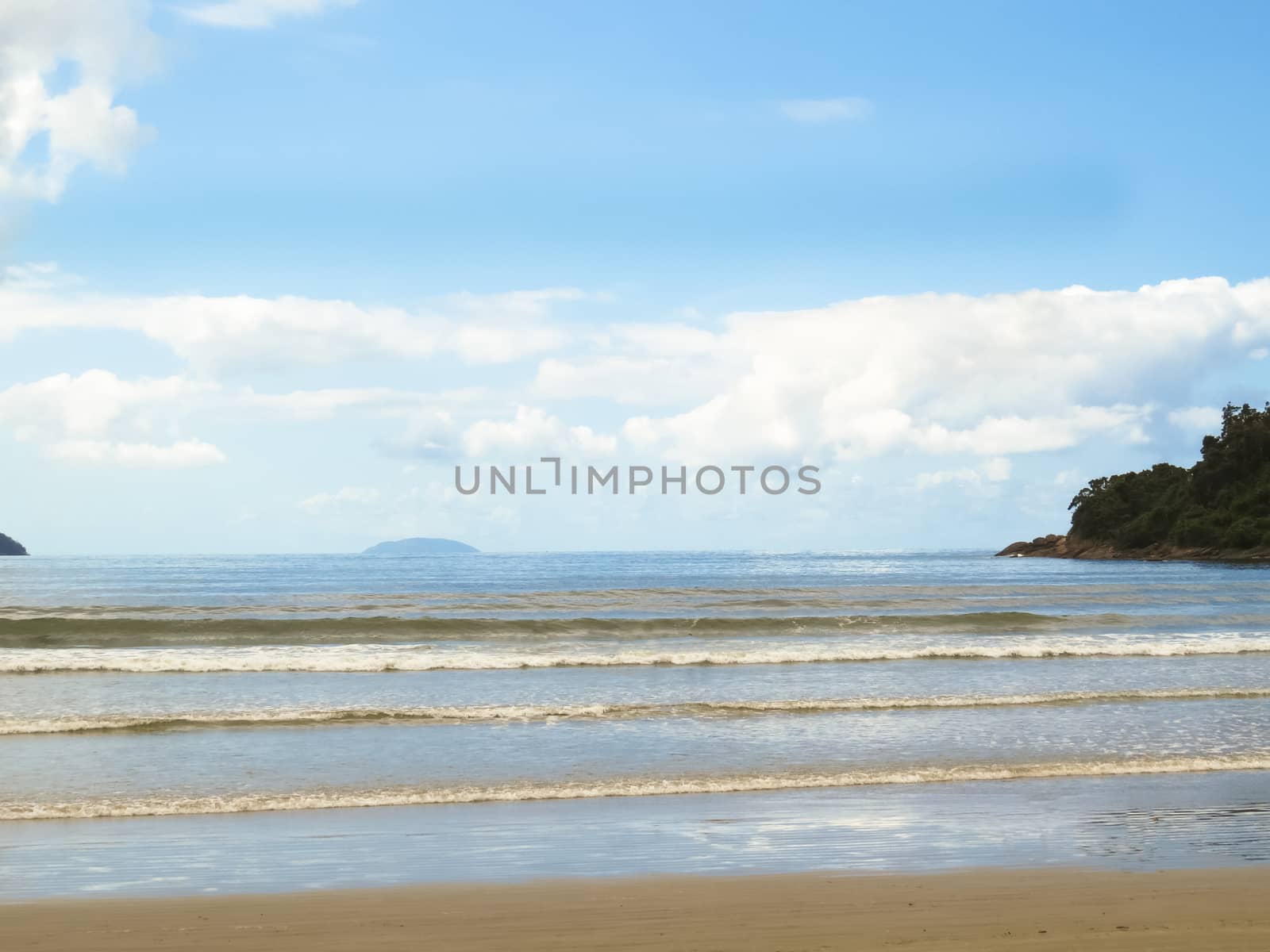 Sun day on beach with waves and island in the background.