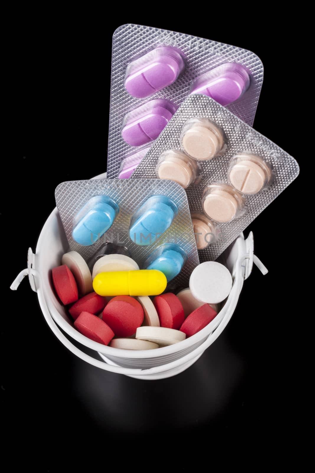 Coloerd pills medicine in a white bucket isolated on black background