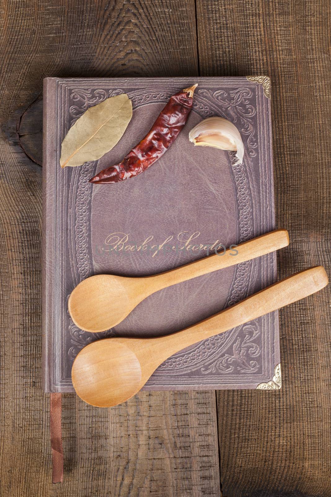 Book of Secrets brown closed cookbook on old wood background with spices and two  spoons