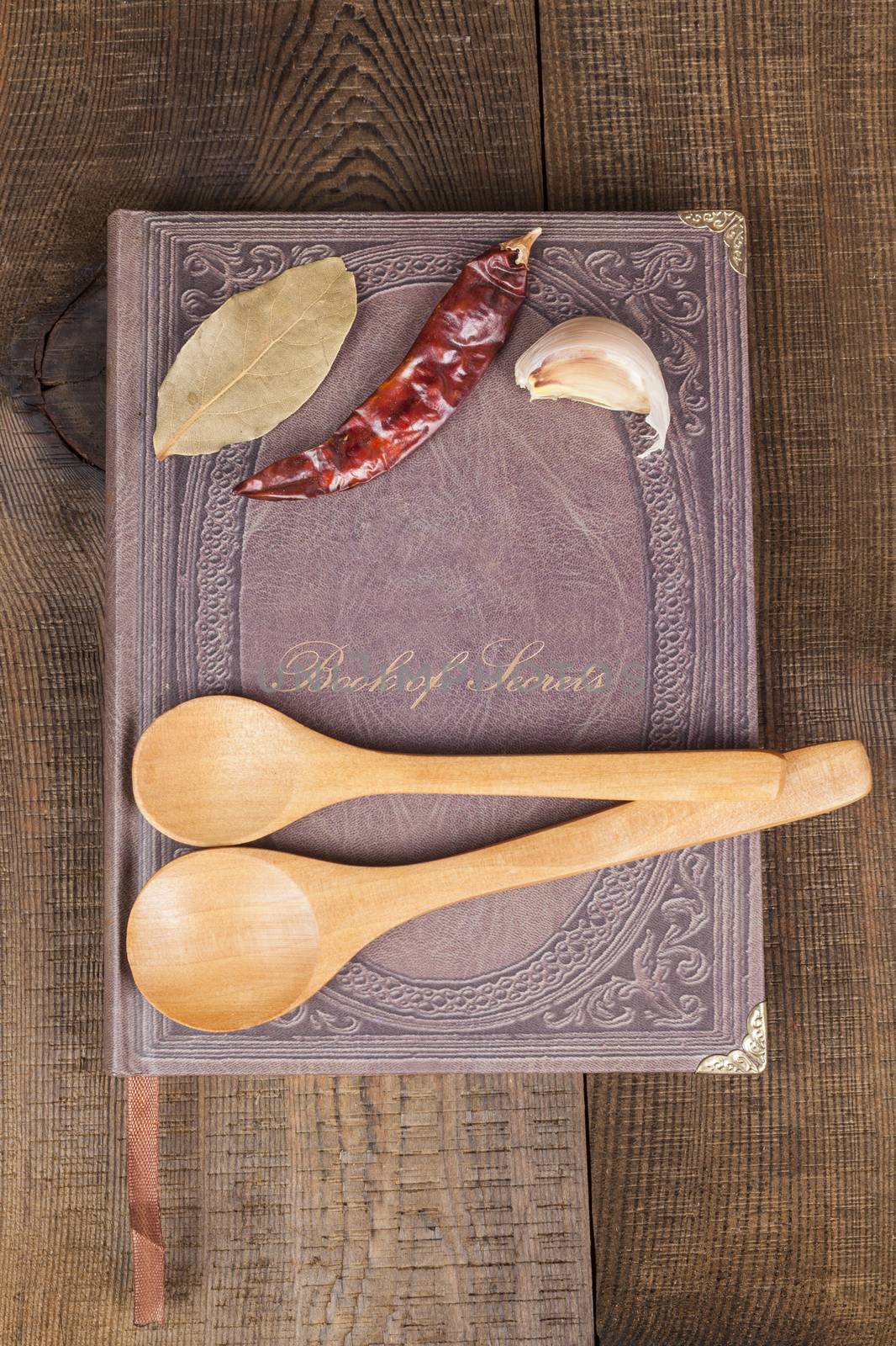 Book of Secrets brown closed cookbook on old wood background with spices and two  spoons