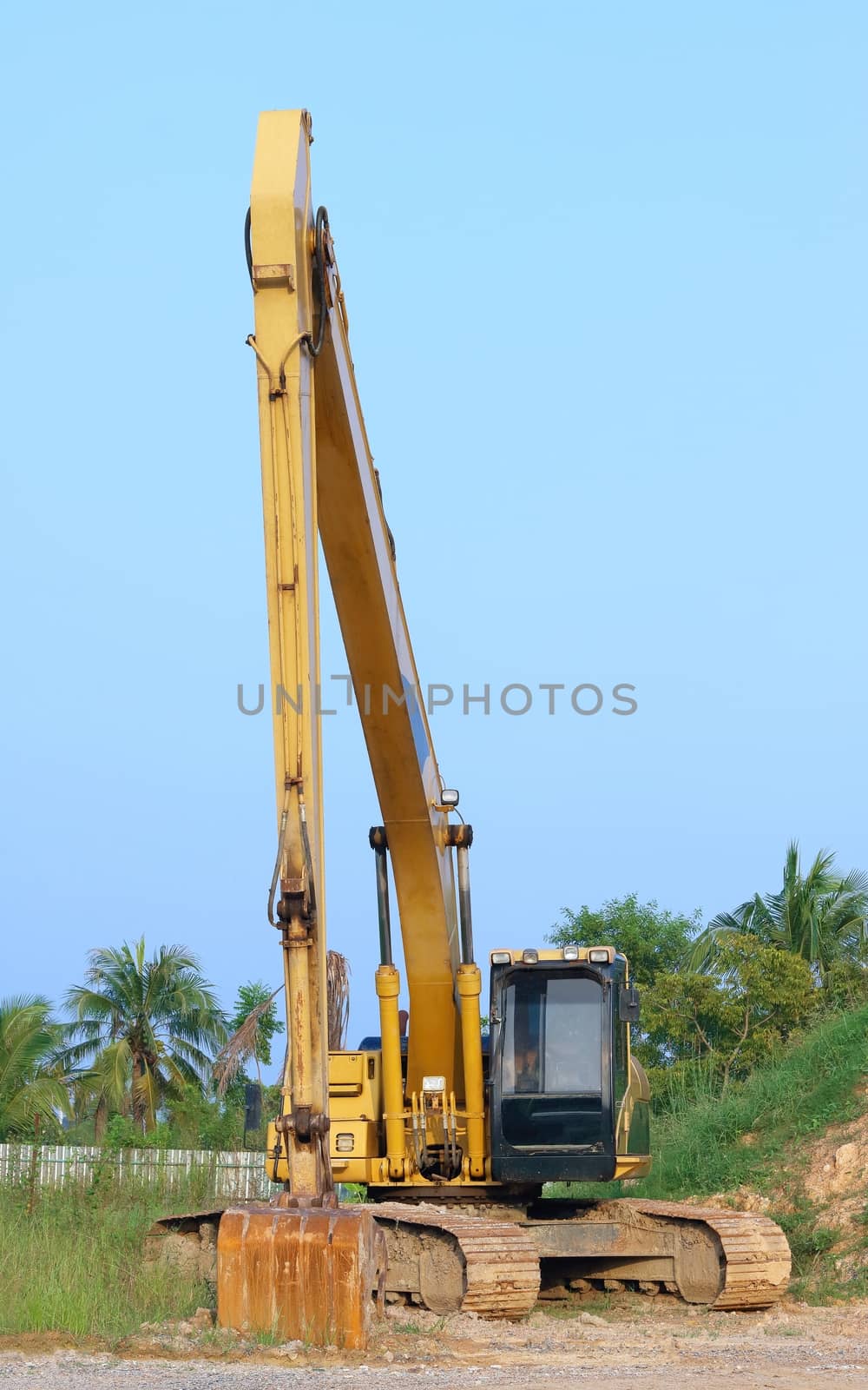Heavy yellow excavator with long boom standing on floor sand.