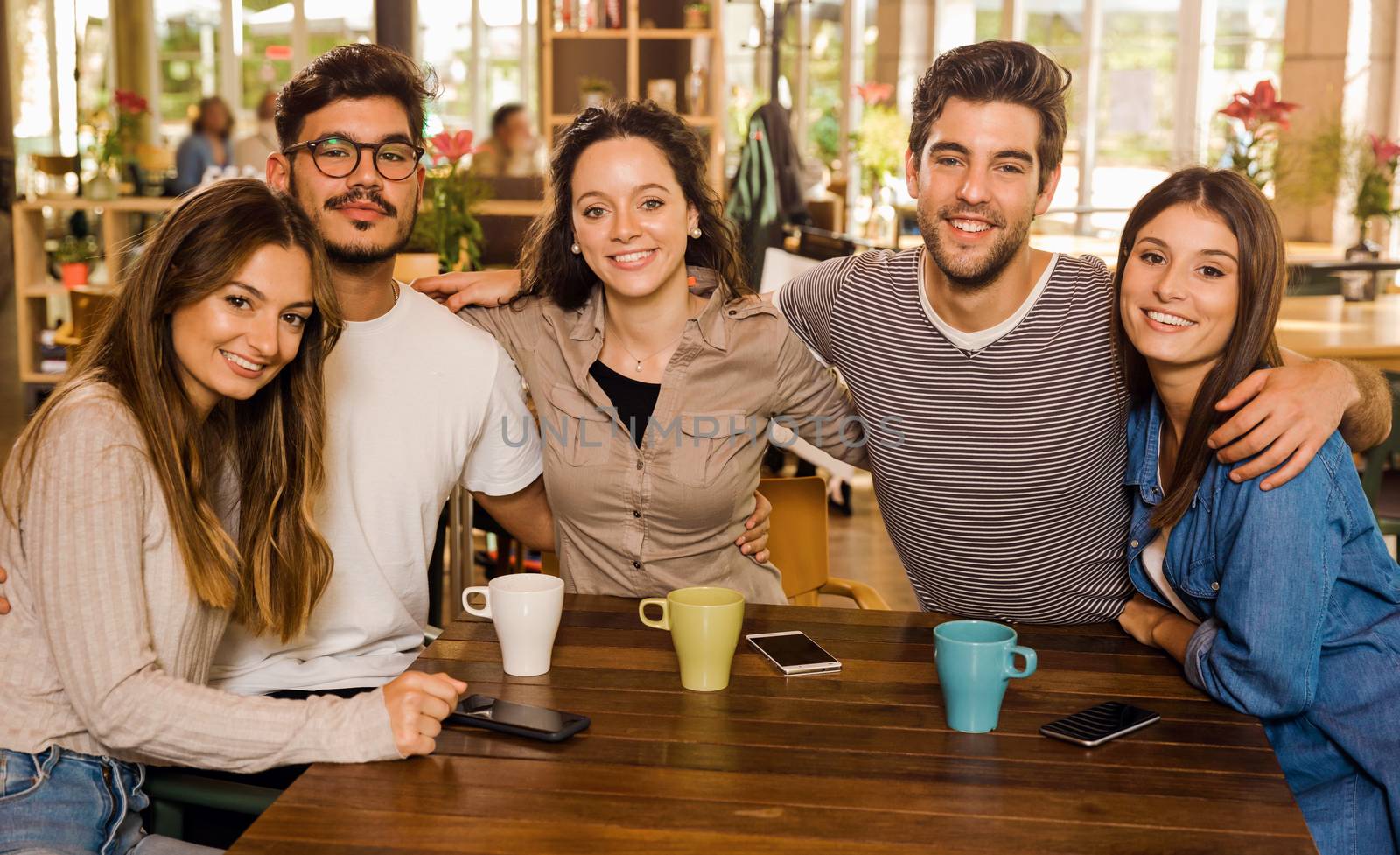 A group of friends looking to the camera and drinking coffee at the cafe