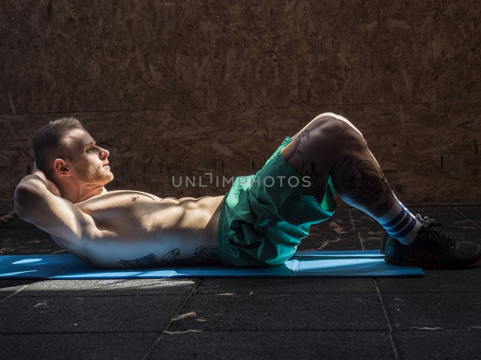 Attractive blond young man shirtless in gym working out, doing exercises for abs.