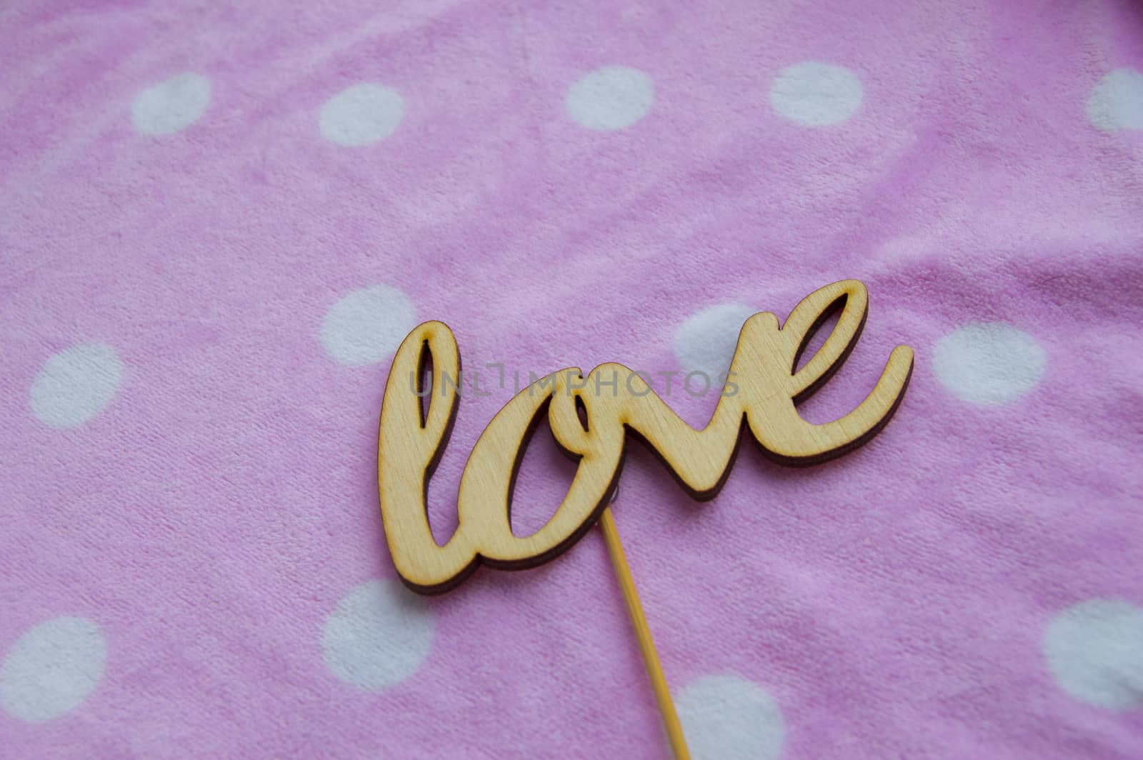 The word love is made of wooden letters on a pink background with white peas. Valentine's day concept, top view.