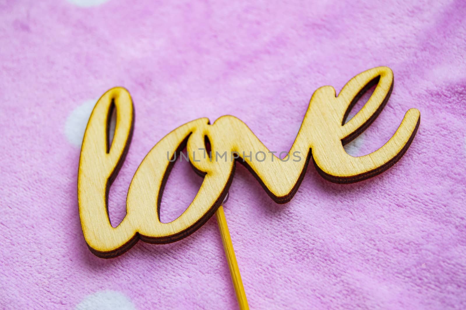 The word love is made of wooden letters on a pink background with white peas. Valentine's day concept, top view.