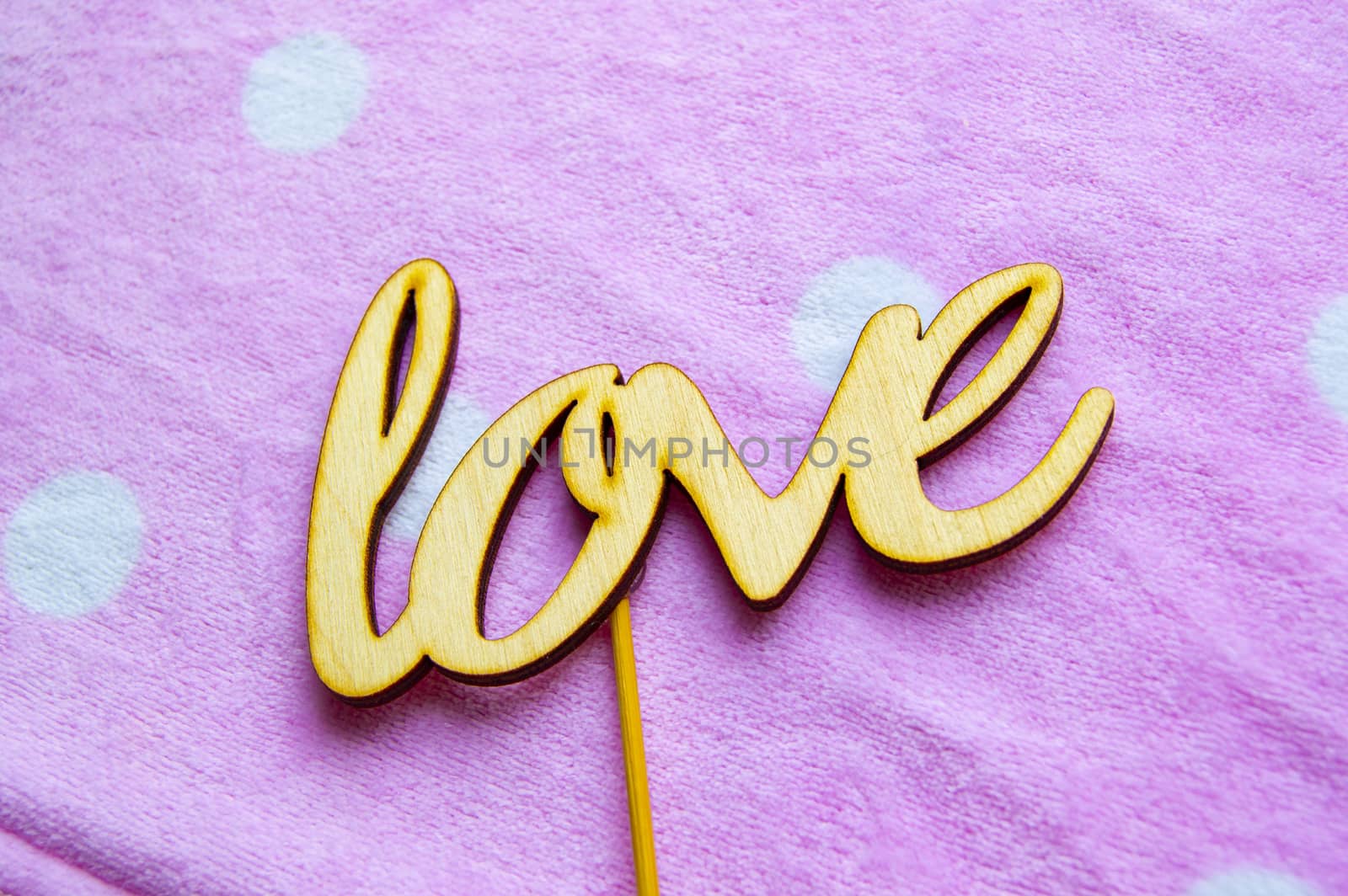 The word love is made of wooden letters on a pink background with white peas. Valentine's day concept, top view.