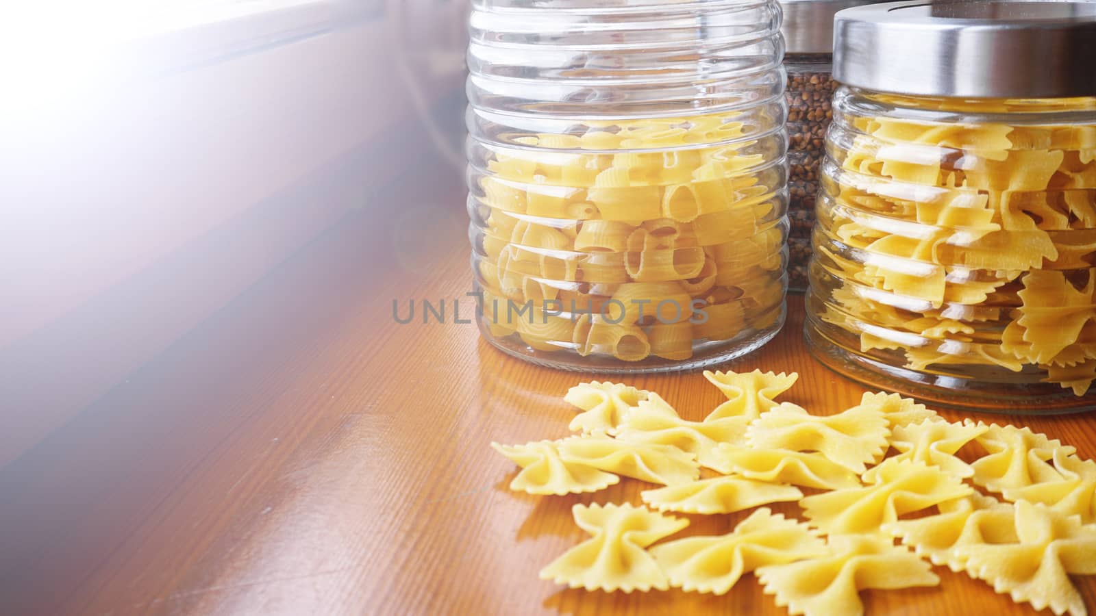 Pasta in the form of bows scattered from glass jar. Italian handmade pasta on the wooden background.