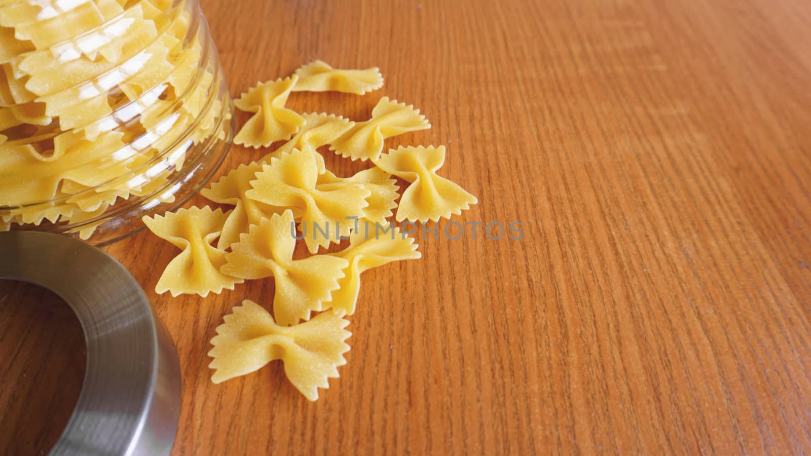 Pasta in the form of bows scattered from glass jar. Italian handmade pasta on the wooden background.