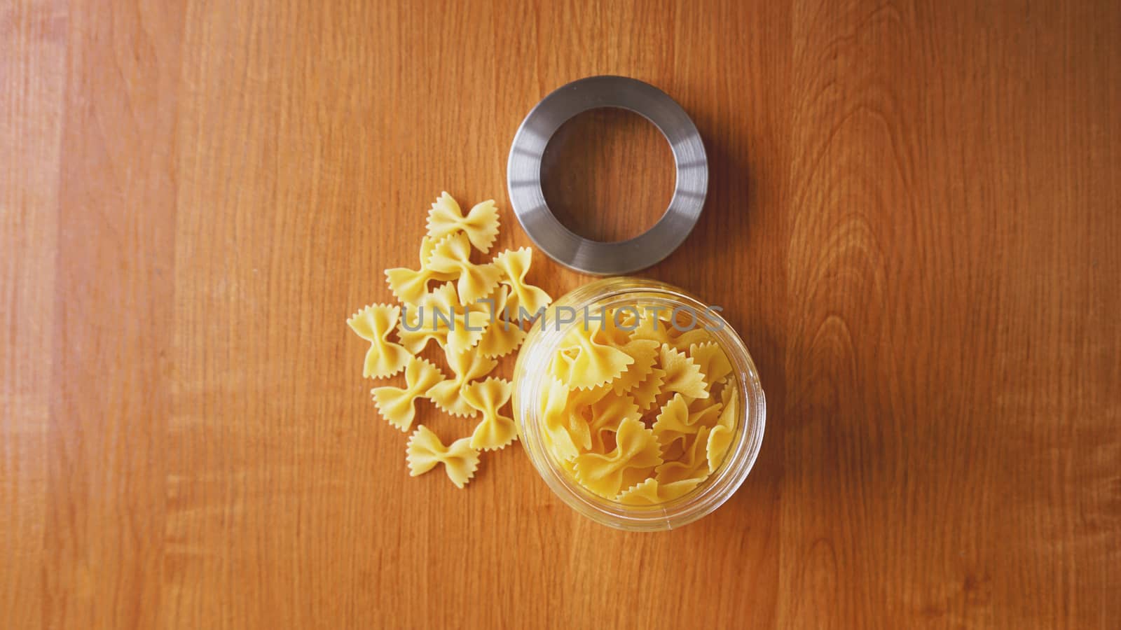 Pasta in the form of bows scattered from glass jar. Italian handmade pasta on the wooden background.