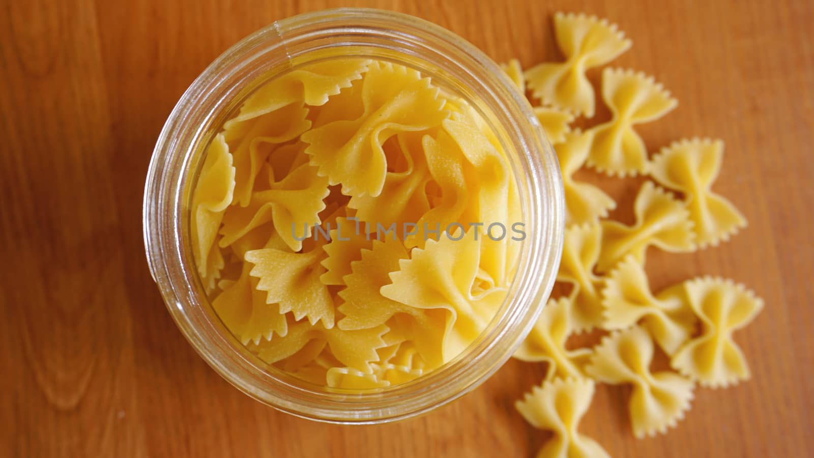 Pasta in the form of bows scattered from glass jar. Italian handmade pasta on the wooden background.