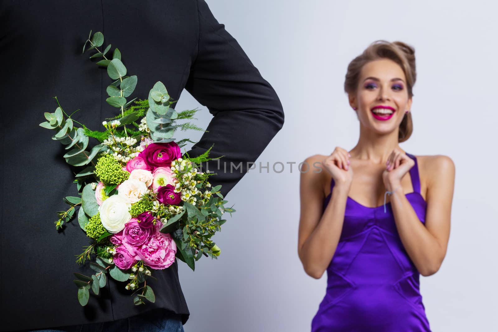 Man brings flowers to woman and hiding them behind back, womanin evening dress is surprised and happy